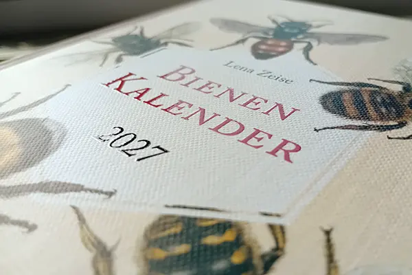 Buchcover gestalten: Fotos des Covers des Bienenkalenders 2027. Durch das einfallende Licht wird der Lack auf dem Titelschriftzug sichtbar.
